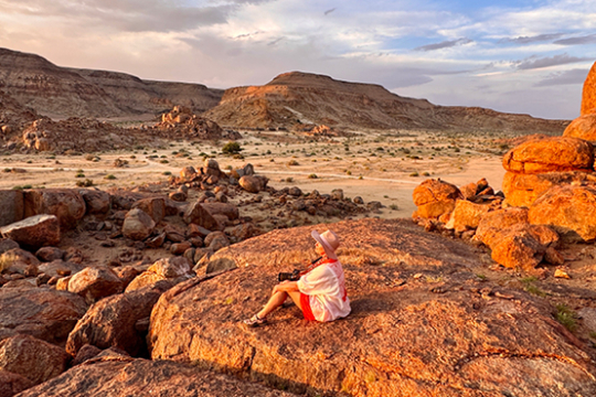Frau sitzt auf einem Felsen in Namibia und genießt die Aussicht auf rote Felsen